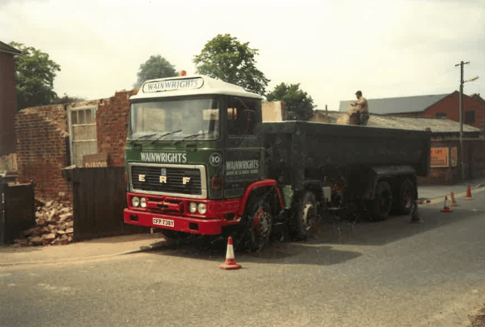Dump truck parked on a street next to a partially demolished brick building, with a person on the truck. Old Ashby de la zouch