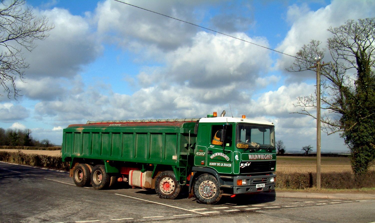 Green wainwrights dump truck on a rural road under a cloudy sky.