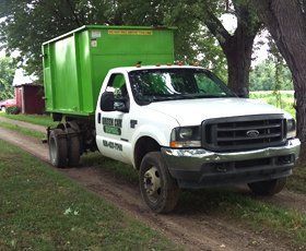 White truck with green dumpster on a dirt road