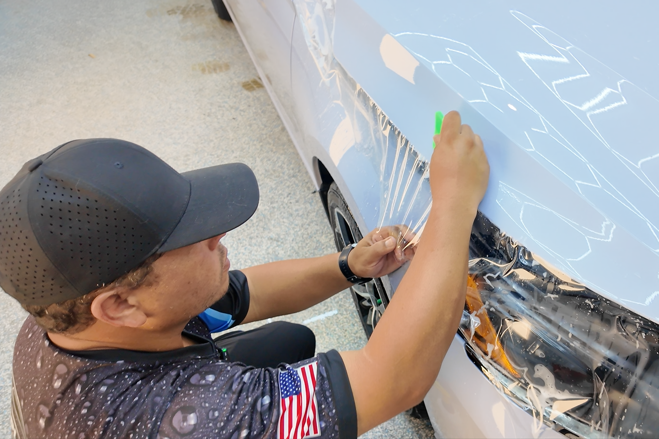 Man applying protective film to a car's hood; interior setting.