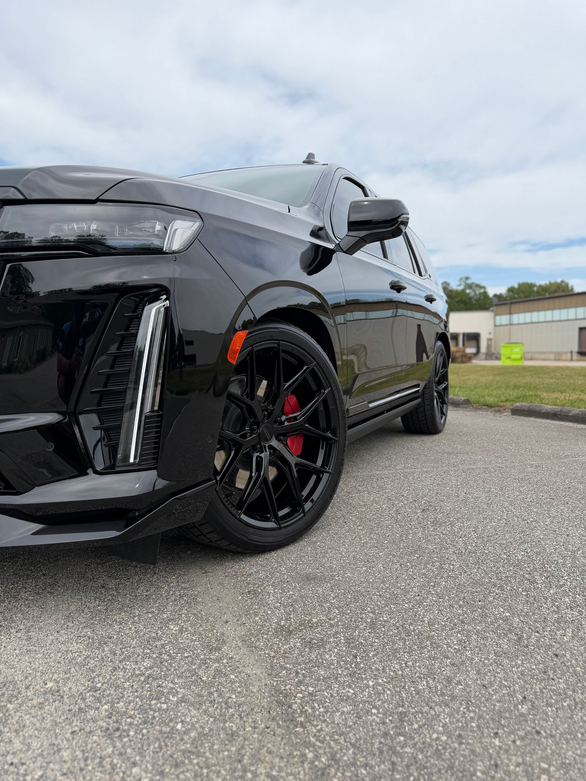 Black sports car with red brake calipers parked on pavement under a cloudy sky.