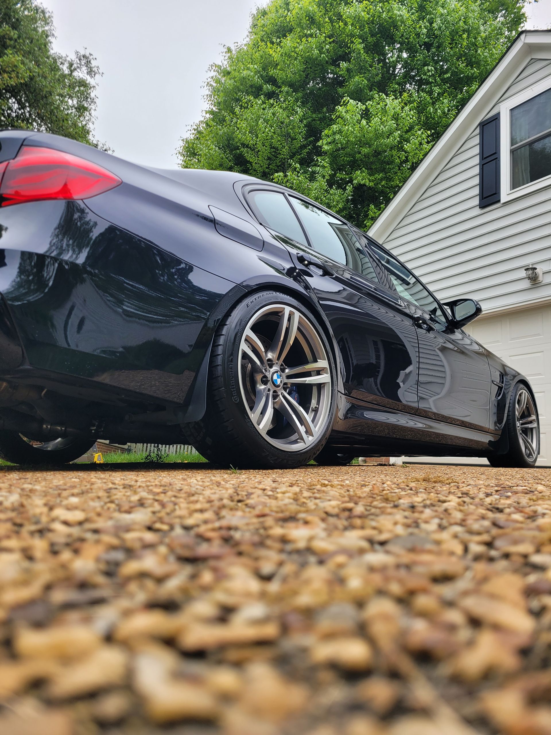 A black car is parked in a gravel driveway in front of a house.