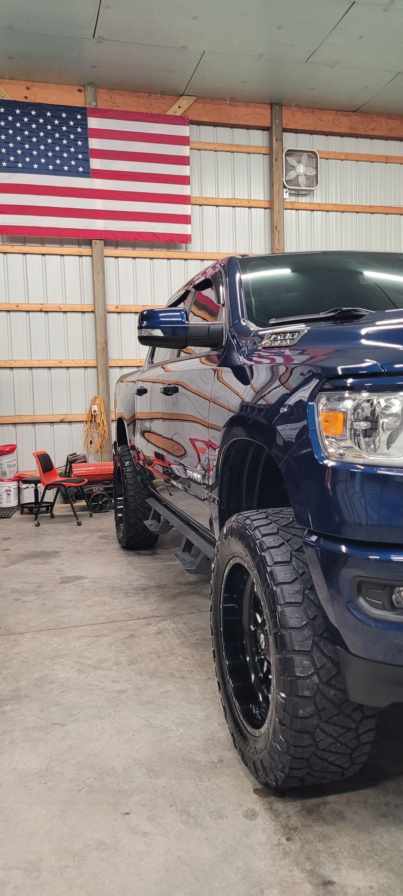 A blue truck is parked in a garage under an american flag.