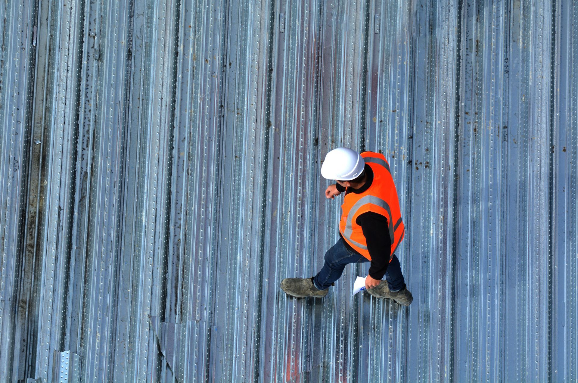 A roof inspector walking across metal panels to assess a commercial structure.