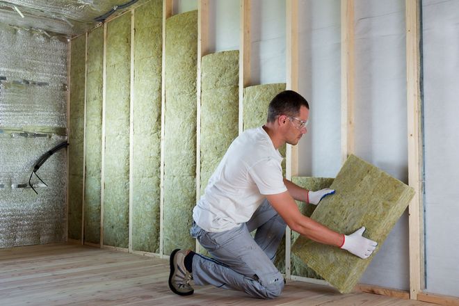 Worker in protective gear insulating rock wool insulation in a wooden frame for a house wall.