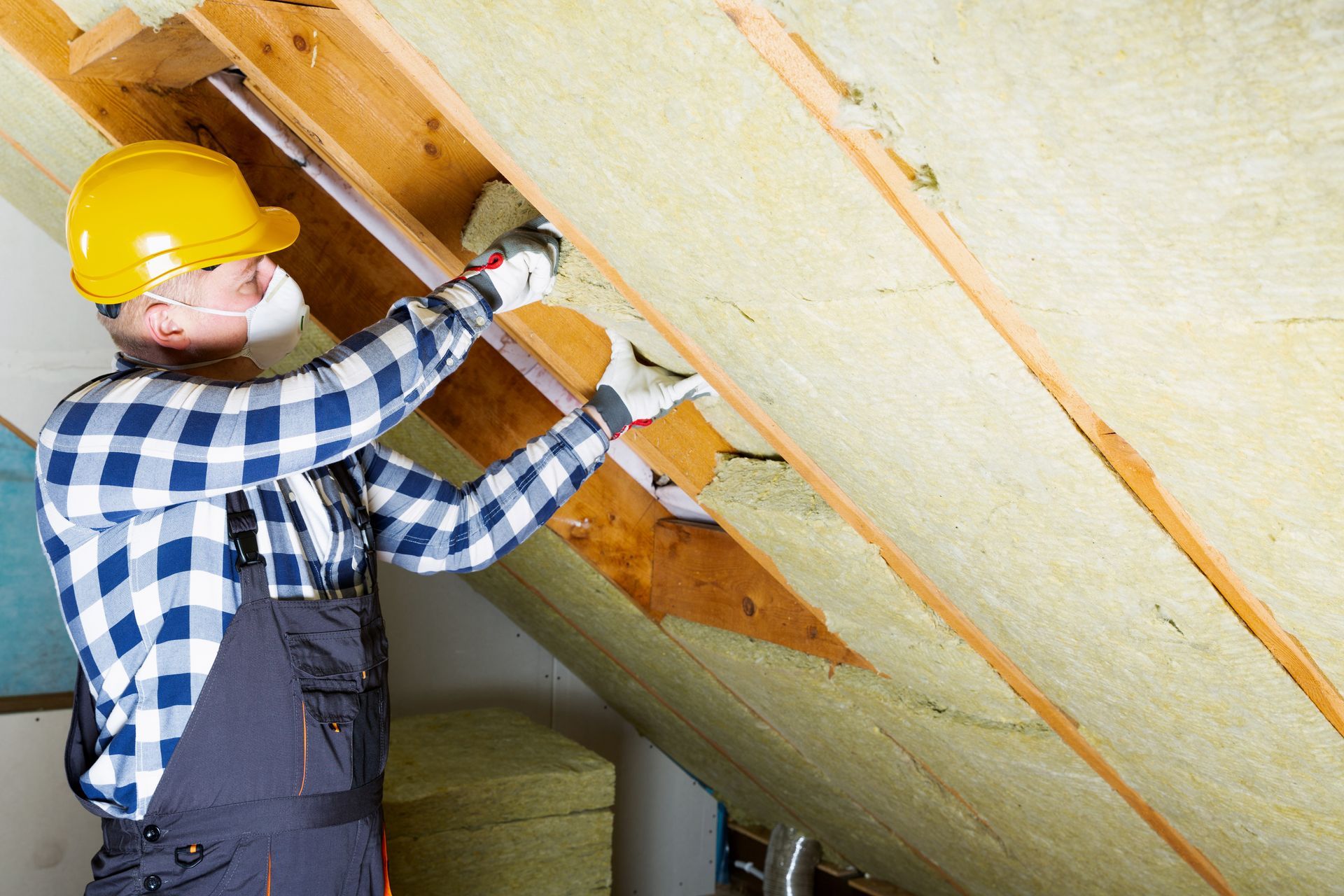Worker installing mineral wool insulation in attic rafters. Worker installing mineral wool insulation in attic rafters.