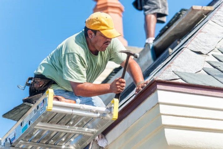 Roofer hammers a copper nail into a piece of slate tile on the roof.