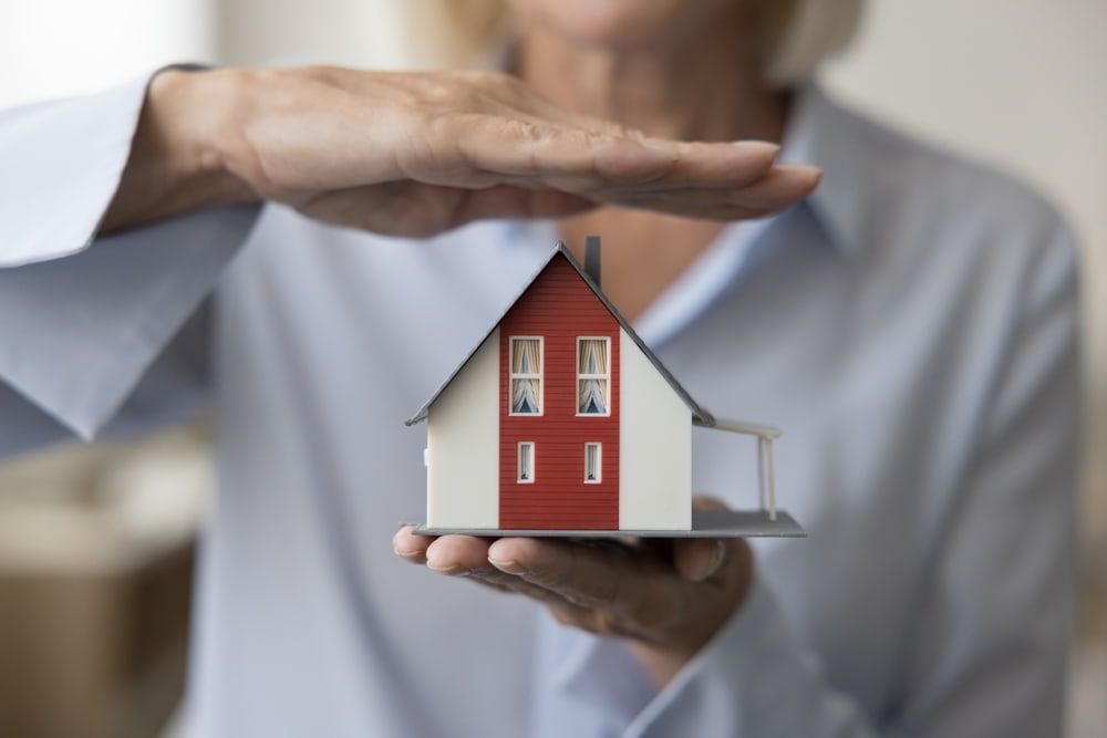 Person holding model house, hands above as if protecting it.