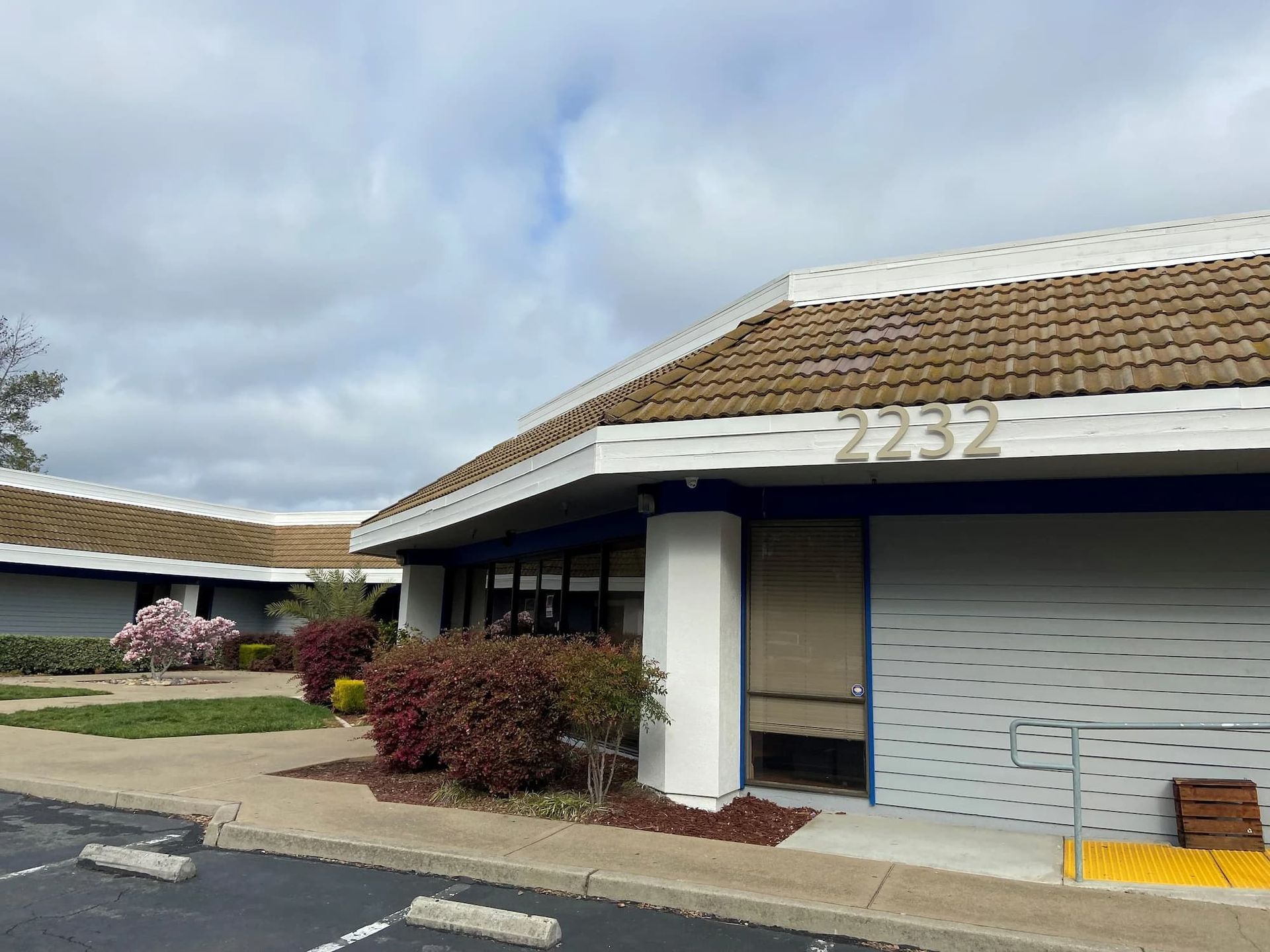 Exterior view of a commercial building with address 2232. Beige tile roof, white trim, blue accents, and overcast sky.