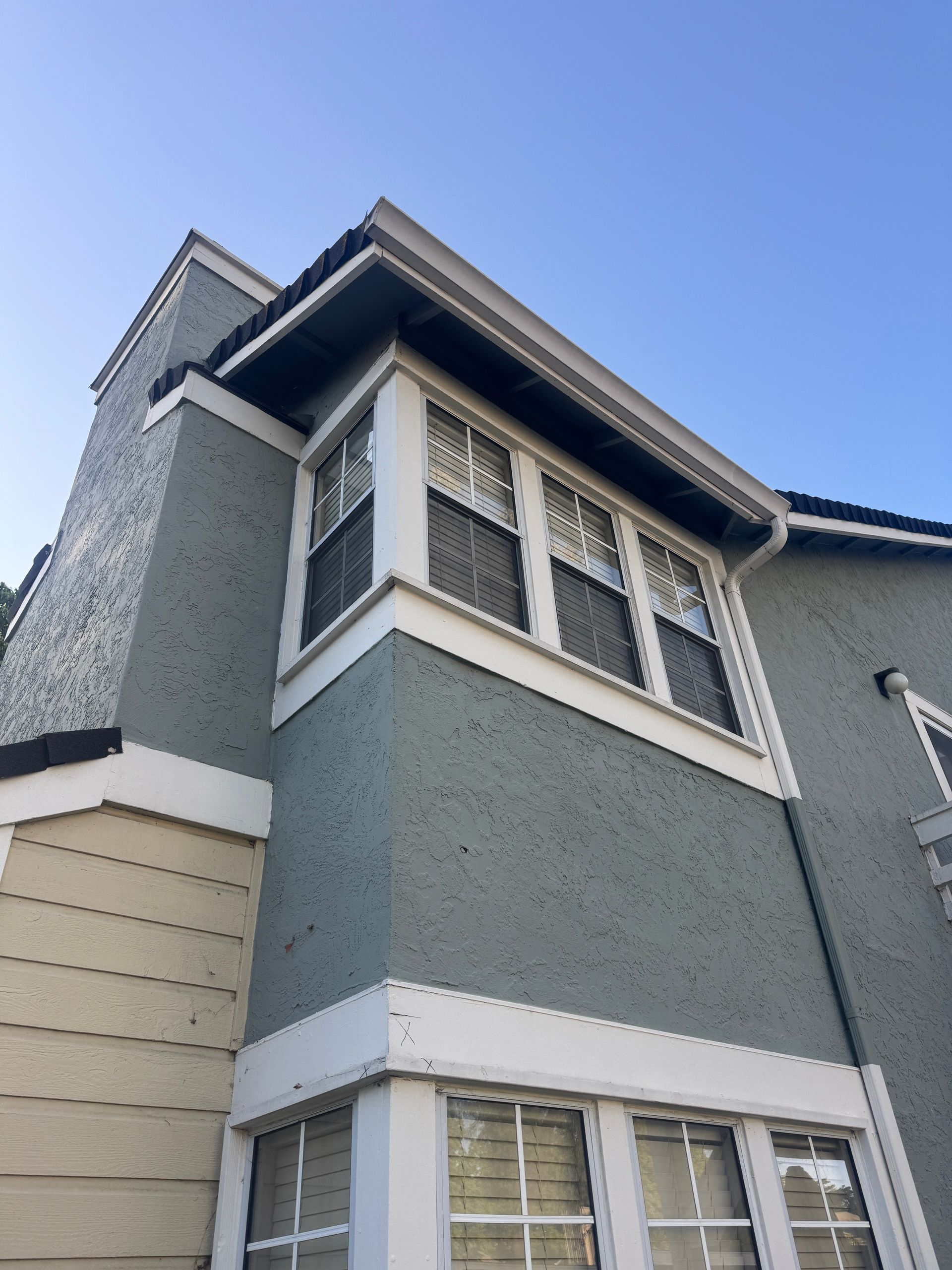 Gray house with porch, shrubs, fence, and blue sky.