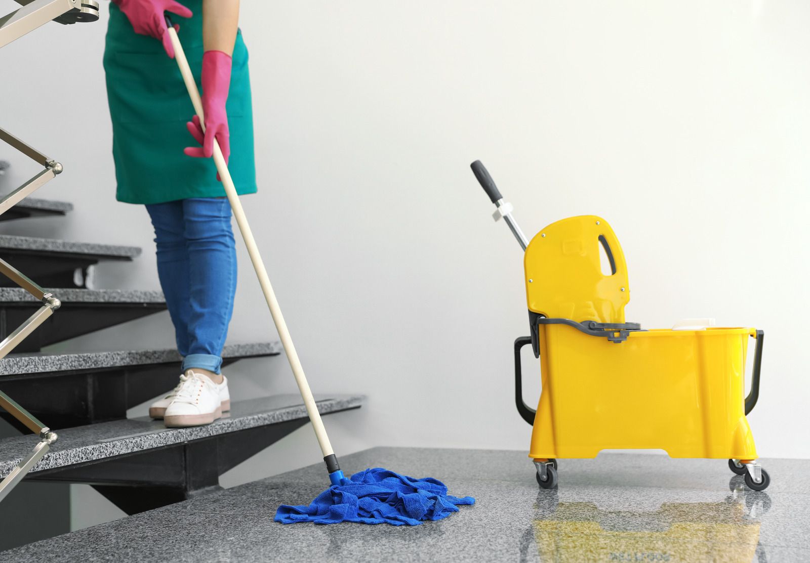 Person mopping a gray staircase with a blue mop, yellow bucket beside.