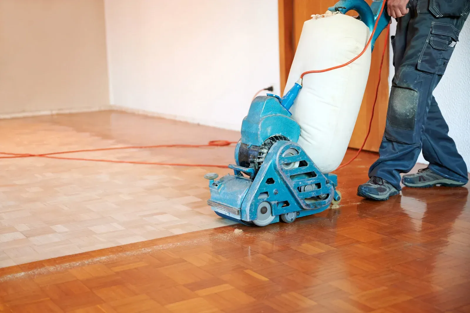 A man is sanding a wooden floor with a machine.