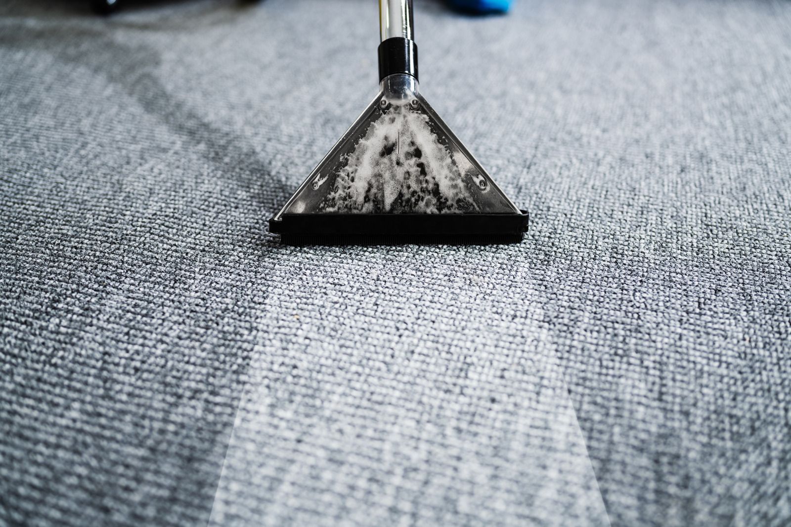Carpet cleaning wand vacuuming a gray carpet, leaving a clean stripe