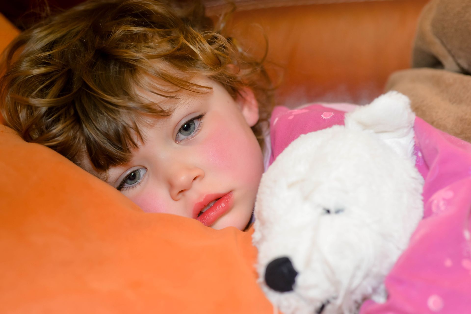 A little girl is laying in bed with a teddy bear.