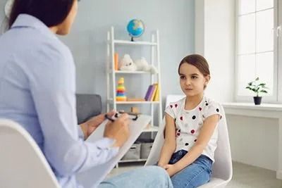 A little girl is sitting in a chair talking to a female psychologist.