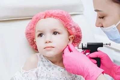 A little girl is getting her ears pierced by a doctor.