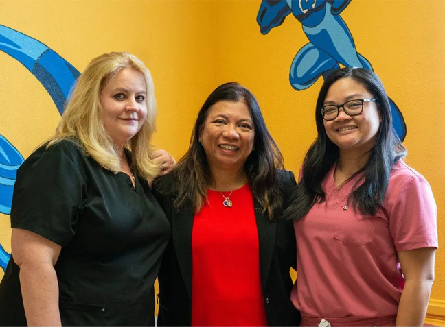 Three women are posing for a picture in front of a yellow wall.