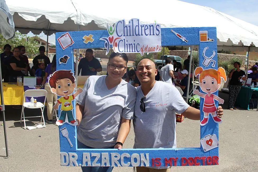 A man and a woman are posing for a picture in front of a children 's clinic photo frame.