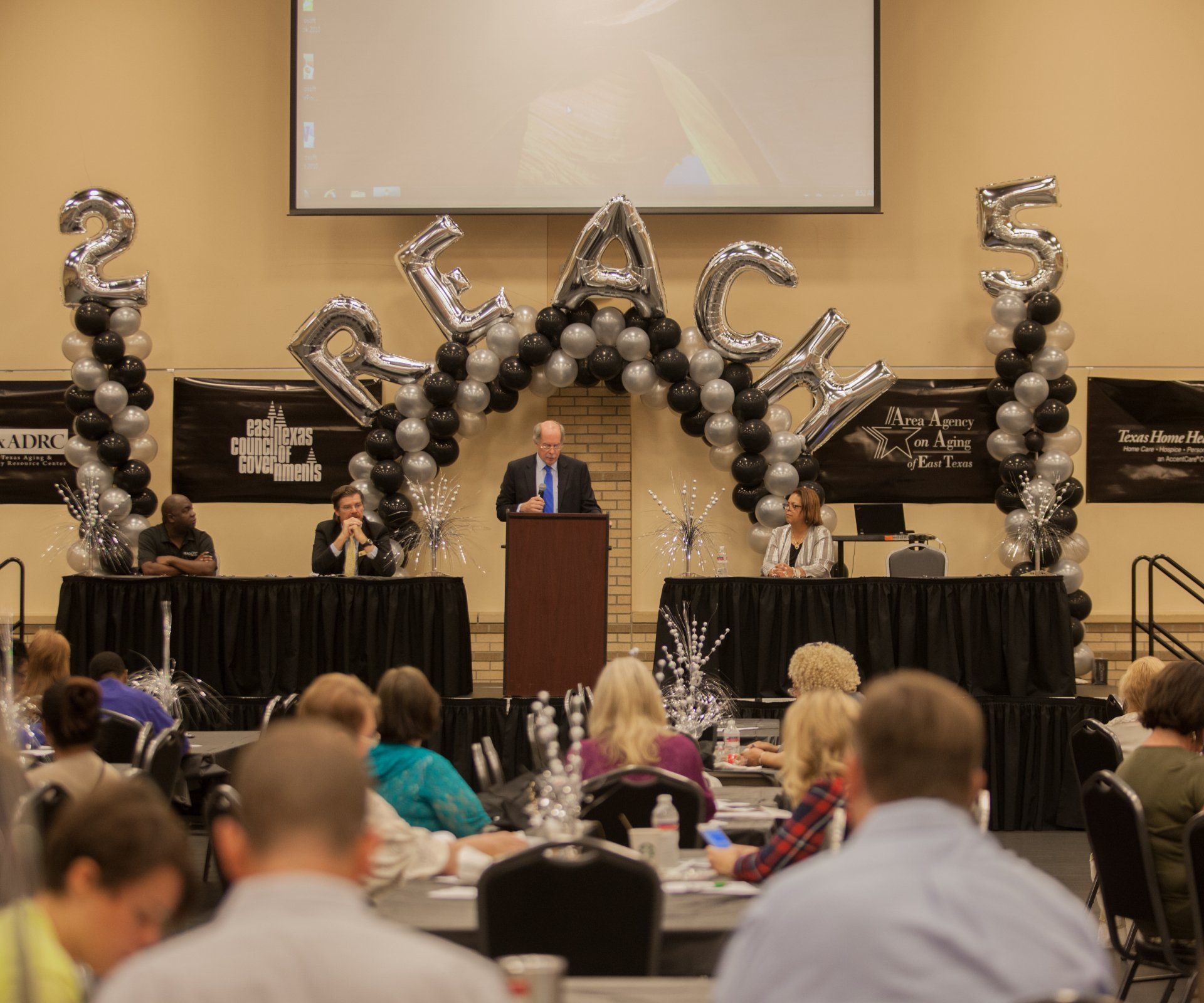 A man is giving a speech in front of balloons that say peace