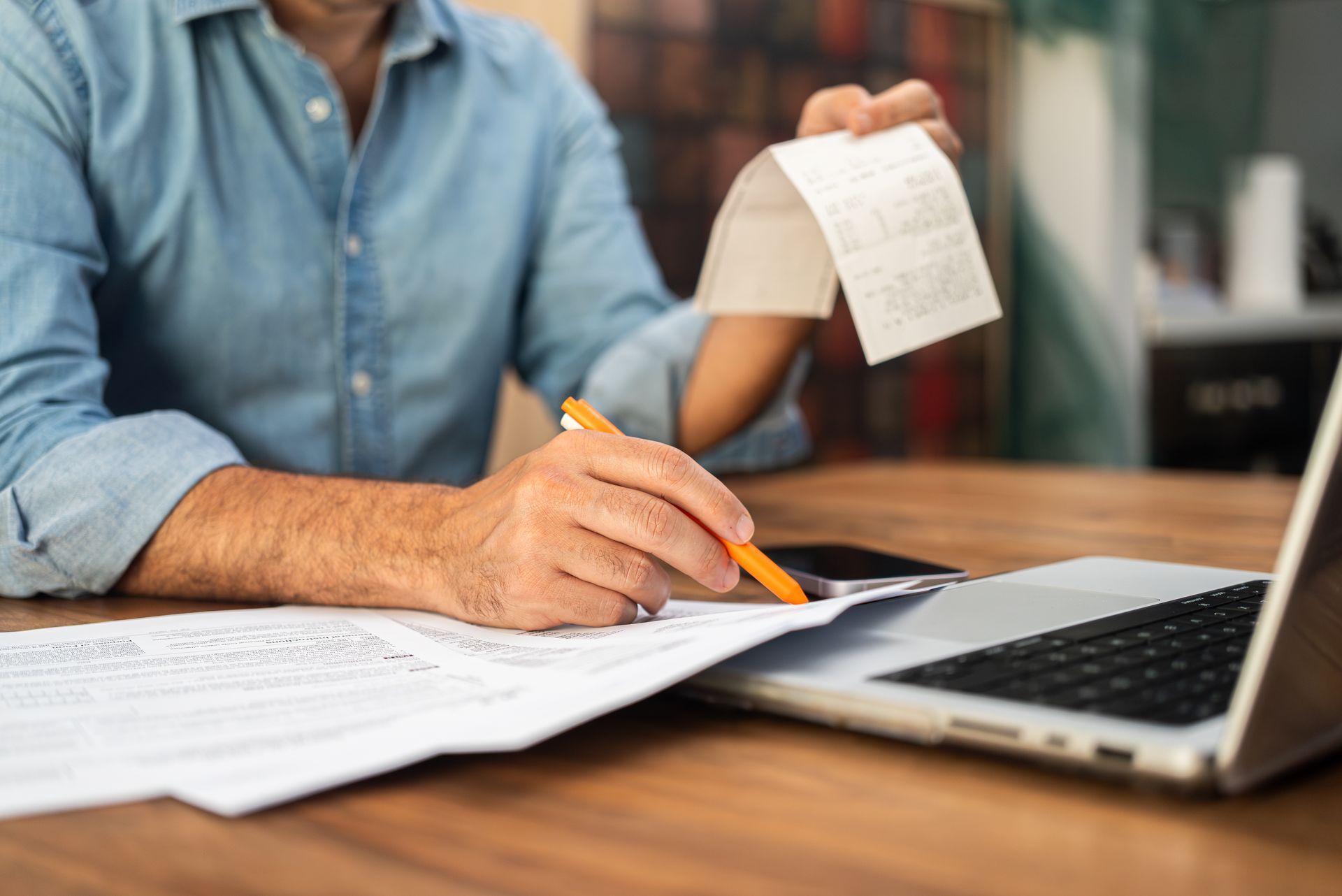 Person reviewing receipts and paperwork at a desk with a laptop.
