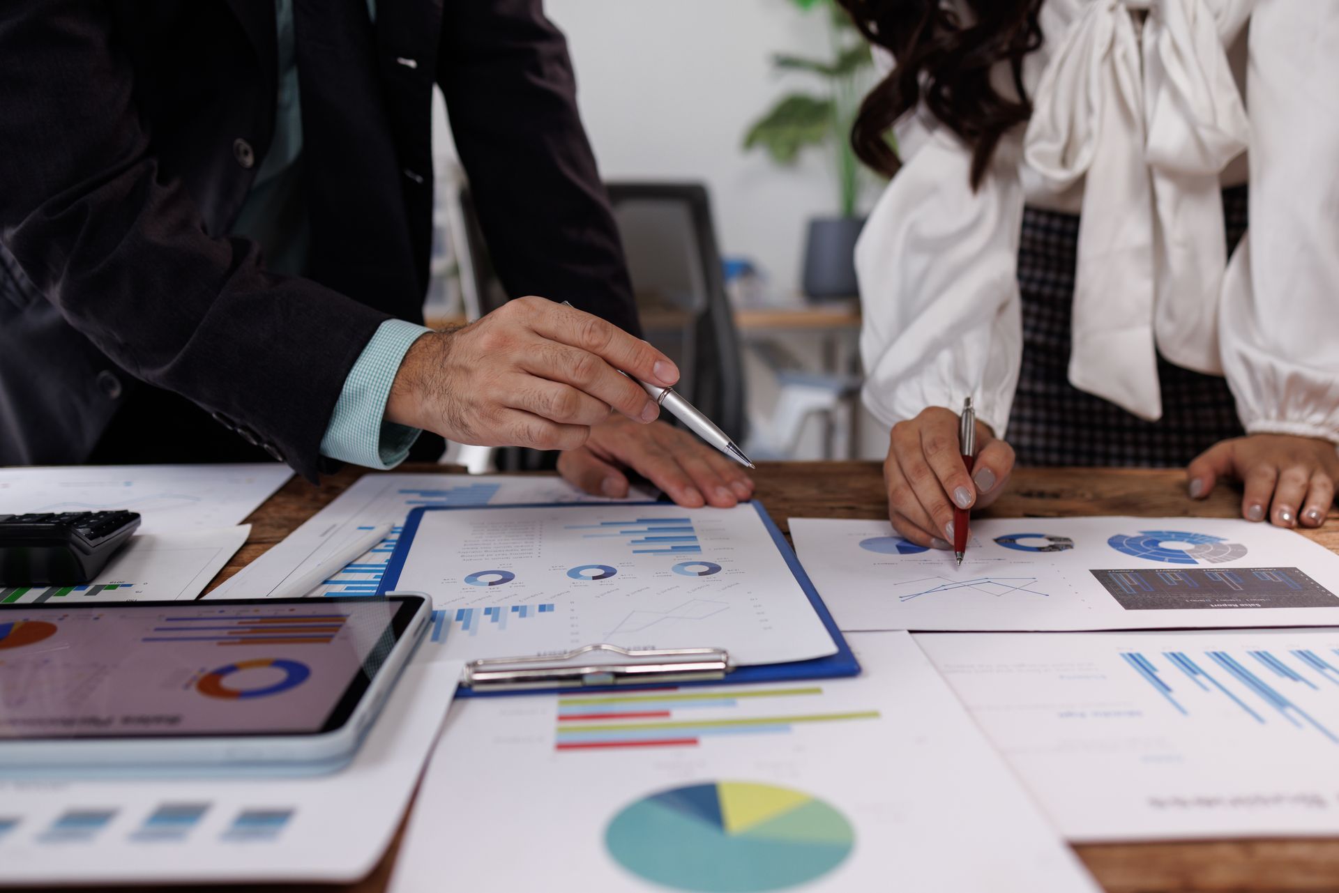 Two people reviewing financial documents, pointing at charts and graphs on a wooden table.