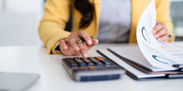 Person in yellow blazer using calculator and reviewing papers with charts.
