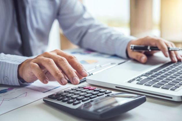 Person's hands using a calculator and laptop, working on financial documents at a desk.