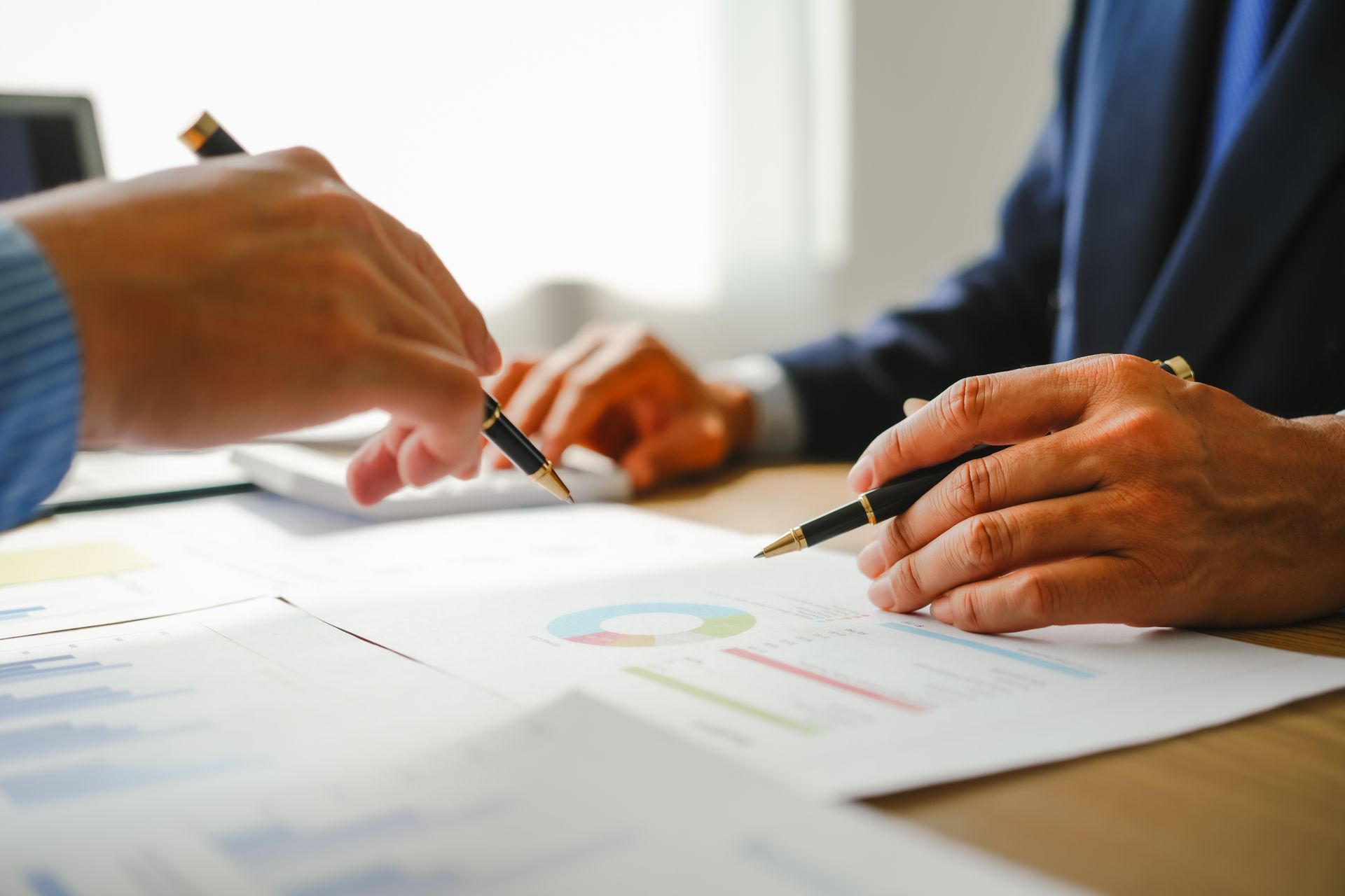 Two people in suits analyzing financial documents with pens.