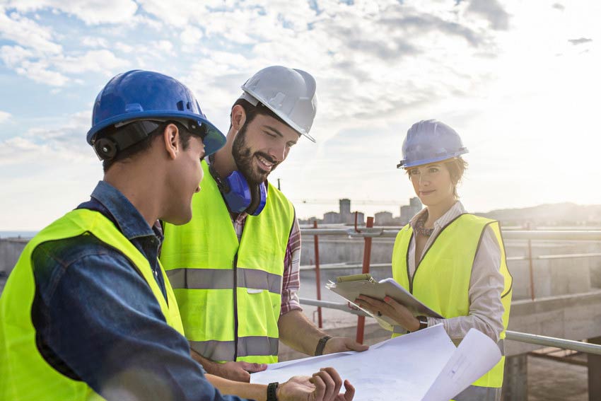 Construction workers and architect looking at blueprints on construction site.