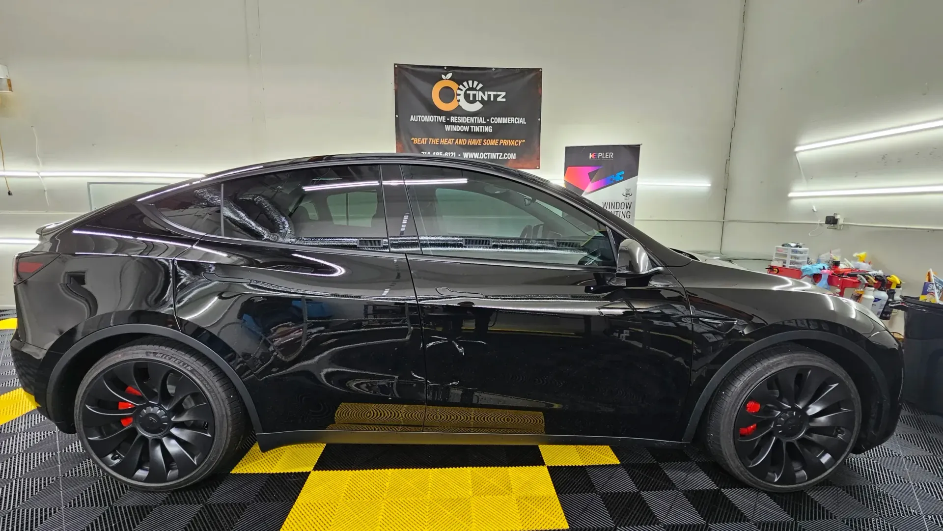Black Tesla Model Y with red brake calipers parked indoors on a checkered floor.