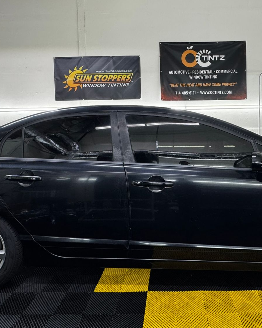 Person applying tinted film to a black car window, inside a garage.