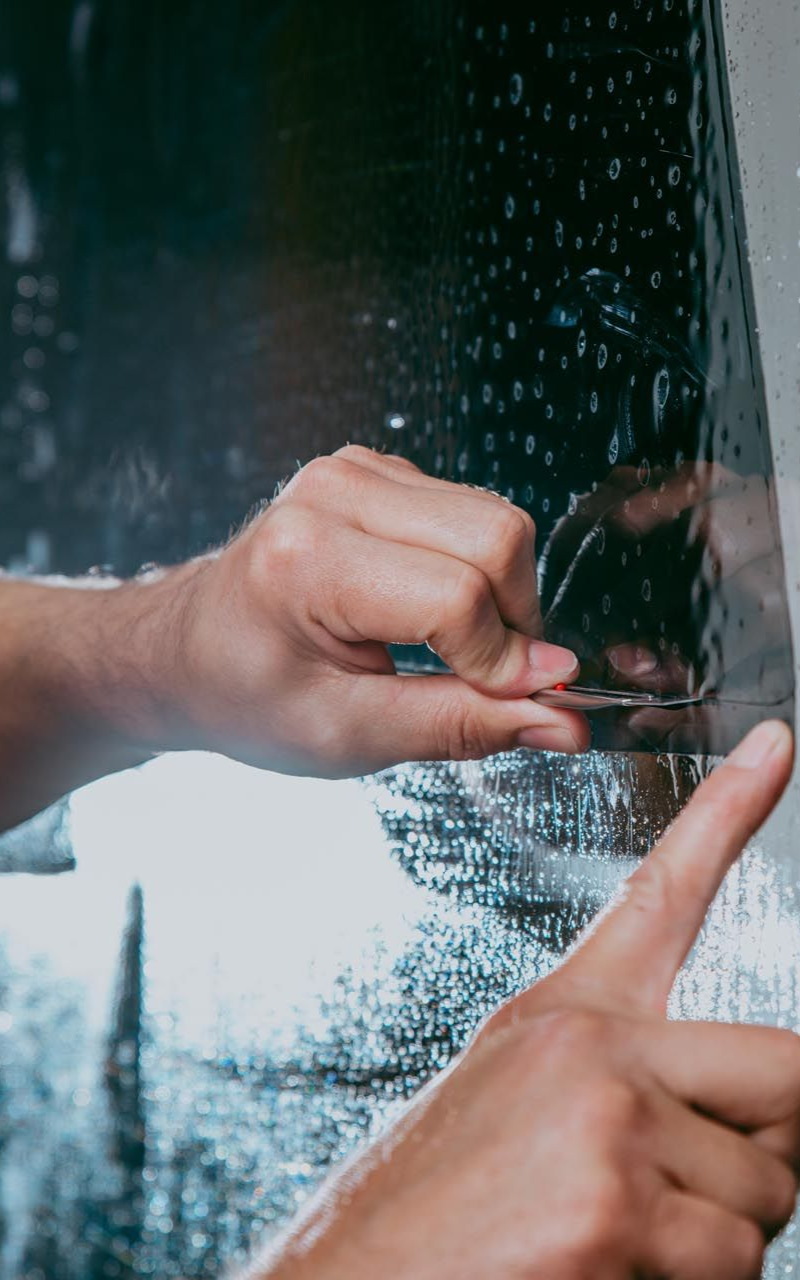 Hands applying window tinting film to glass.