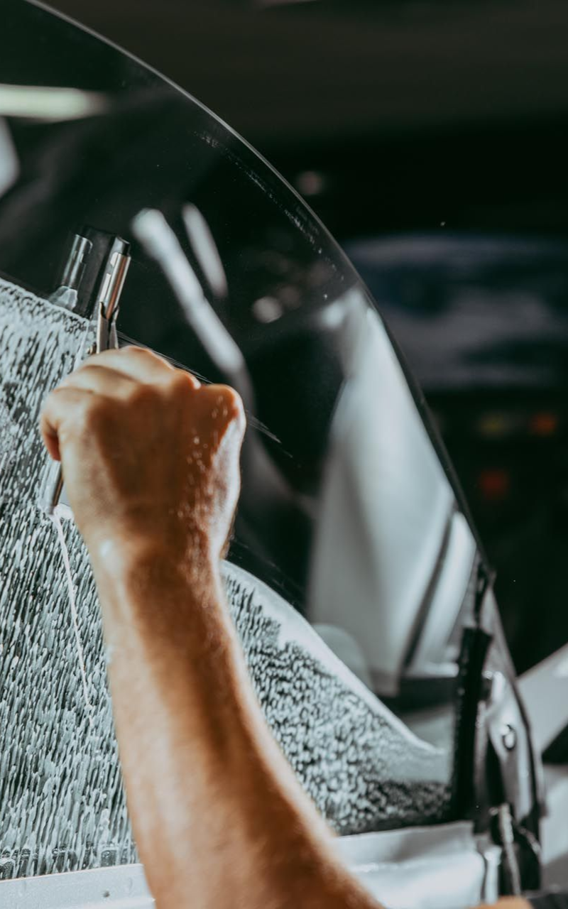 Person's hand applying tint to a car window with a squeegee. The car is inside a garage.