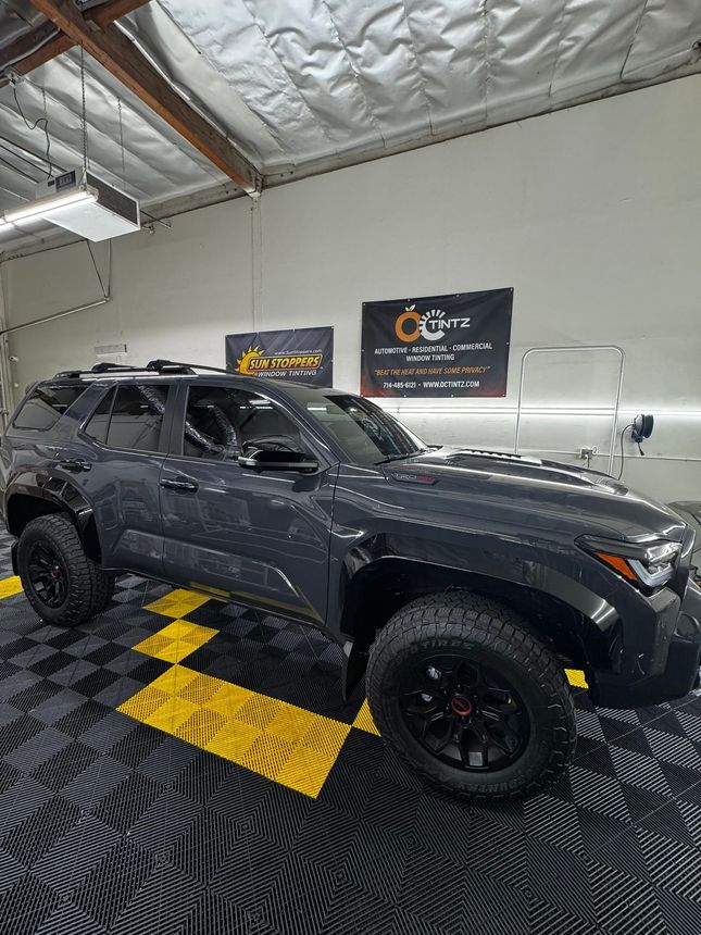 Dark gray SUV with black wheels on a black/yellow checkered floor in a garage setting.