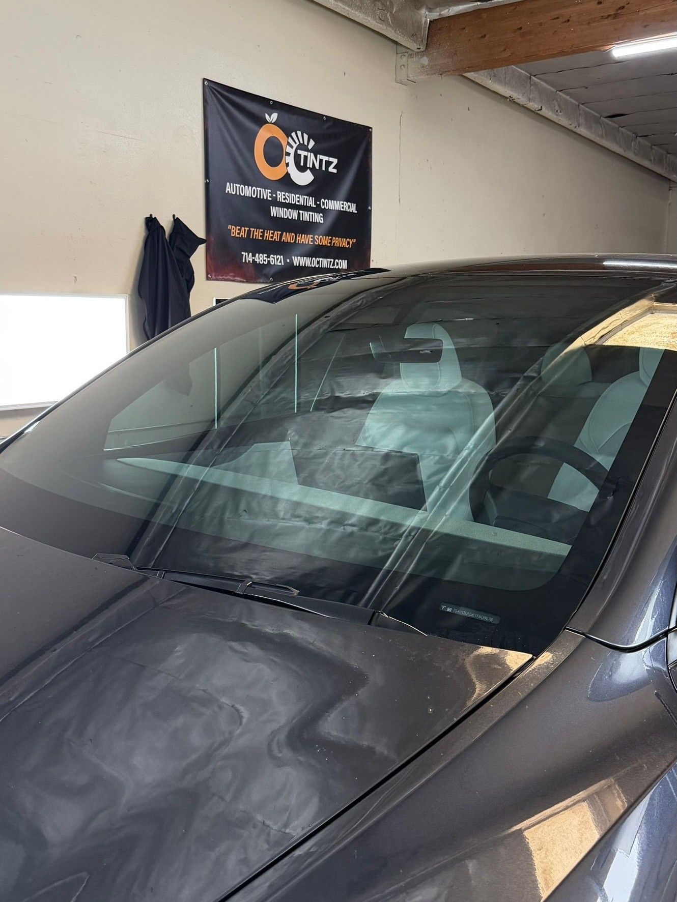 Person in black gloves applying film to a car window with spray, in a garage.