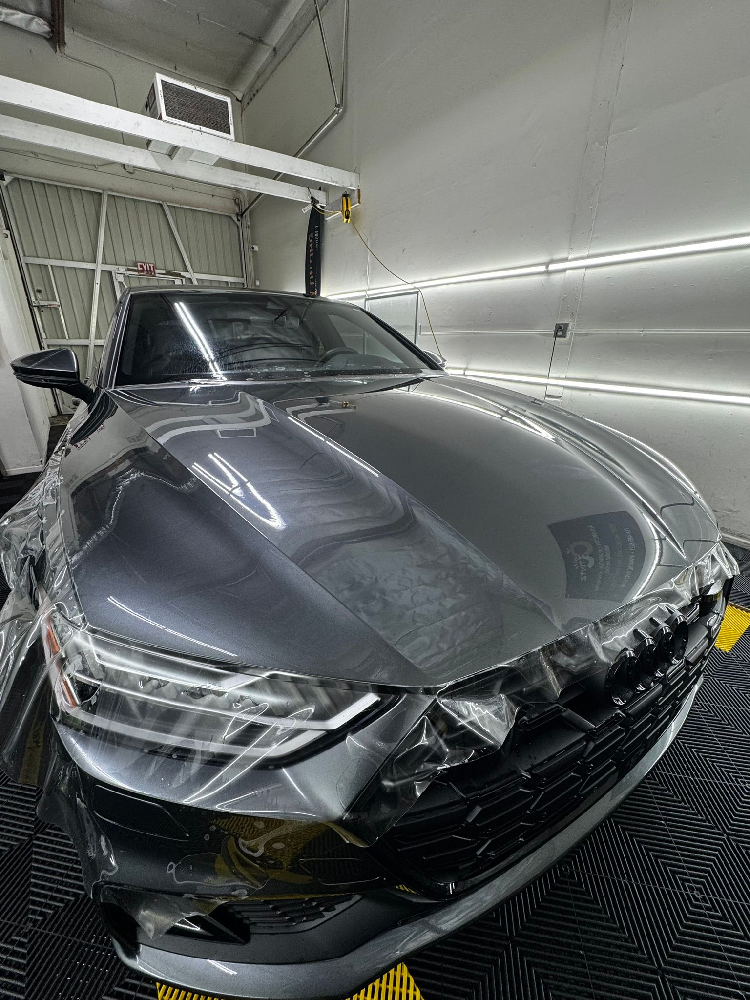 Gray car covered in protective film, inside a garage for detailing.