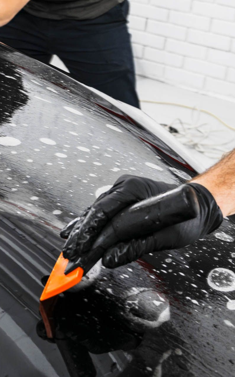 Person applying film to a car hood with a squeegee and gloves.