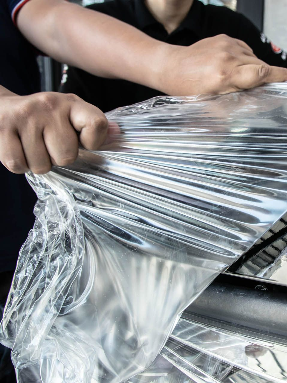 Hands wrapping a metallic object in clear plastic wrap.