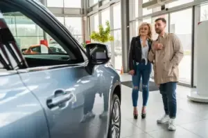 Couple looking at a silver car in a showroom, man pointing, woman wearing jeans.