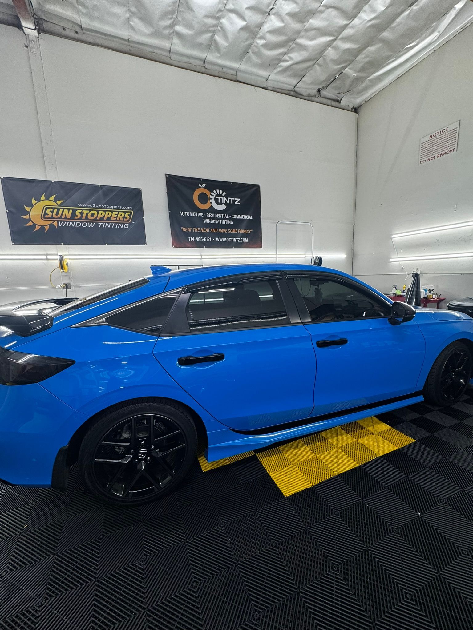 Blue Honda Civic sedan with black accents, parked in a garage on a yellow platform.