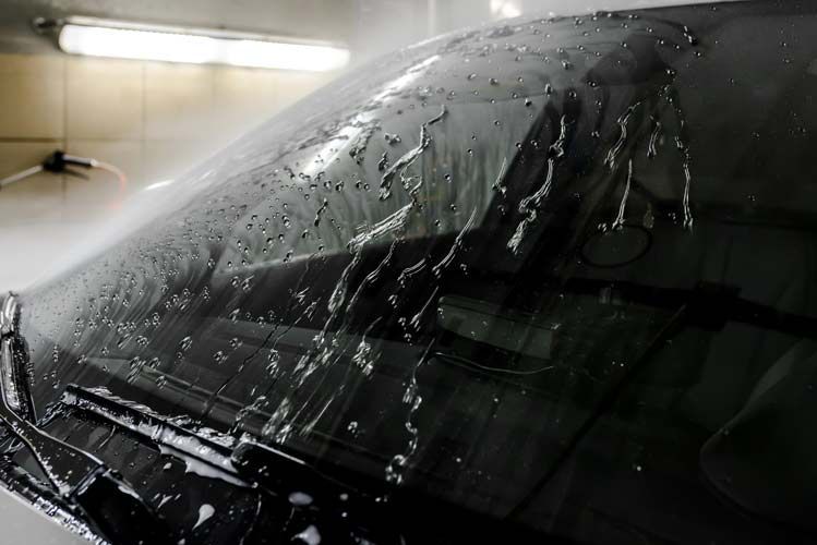 Windshield of a car being sprayed with water, likely for cleaning.