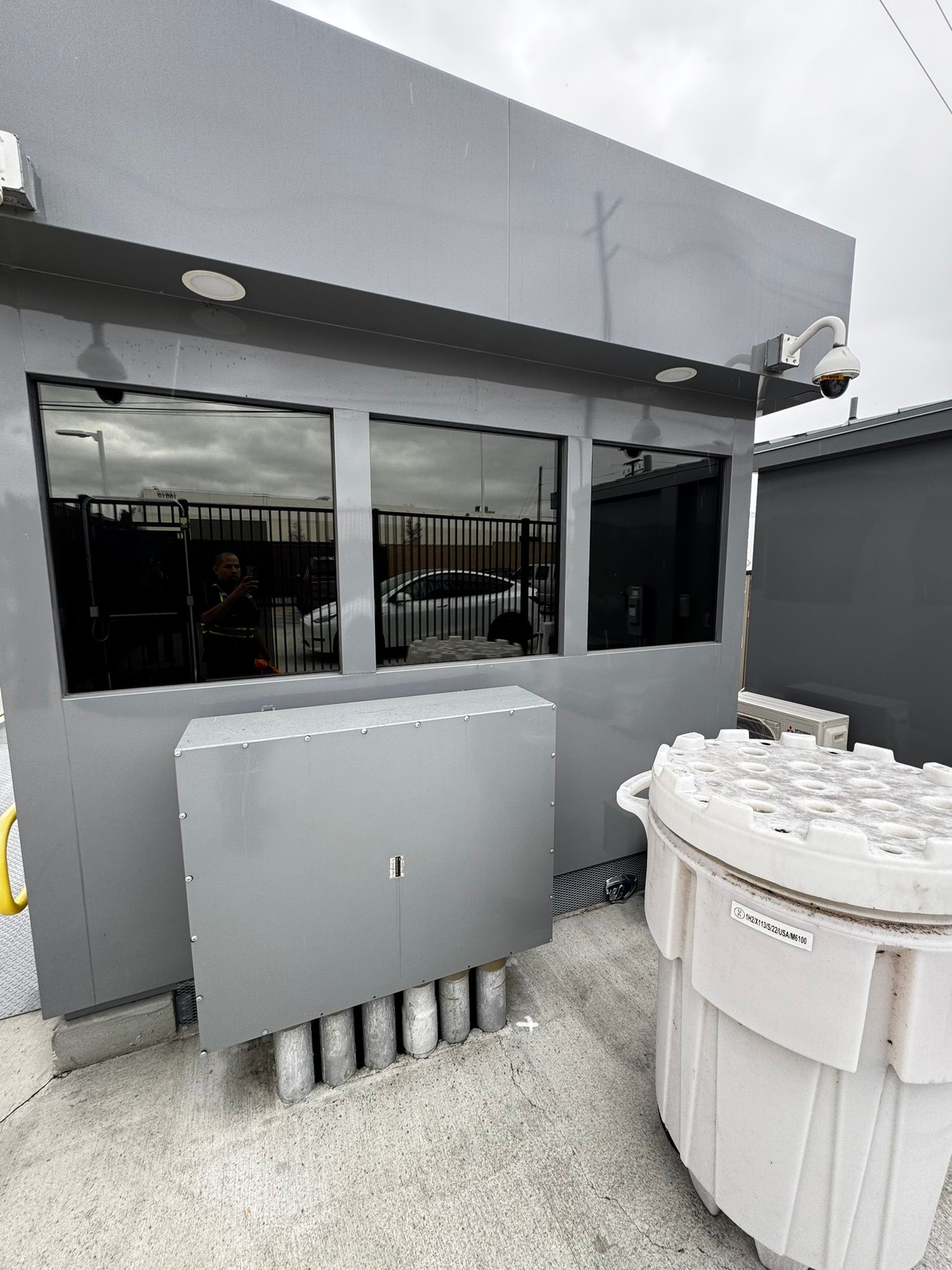 Gray industrial building with dark windows, security cameras, and electrical box.