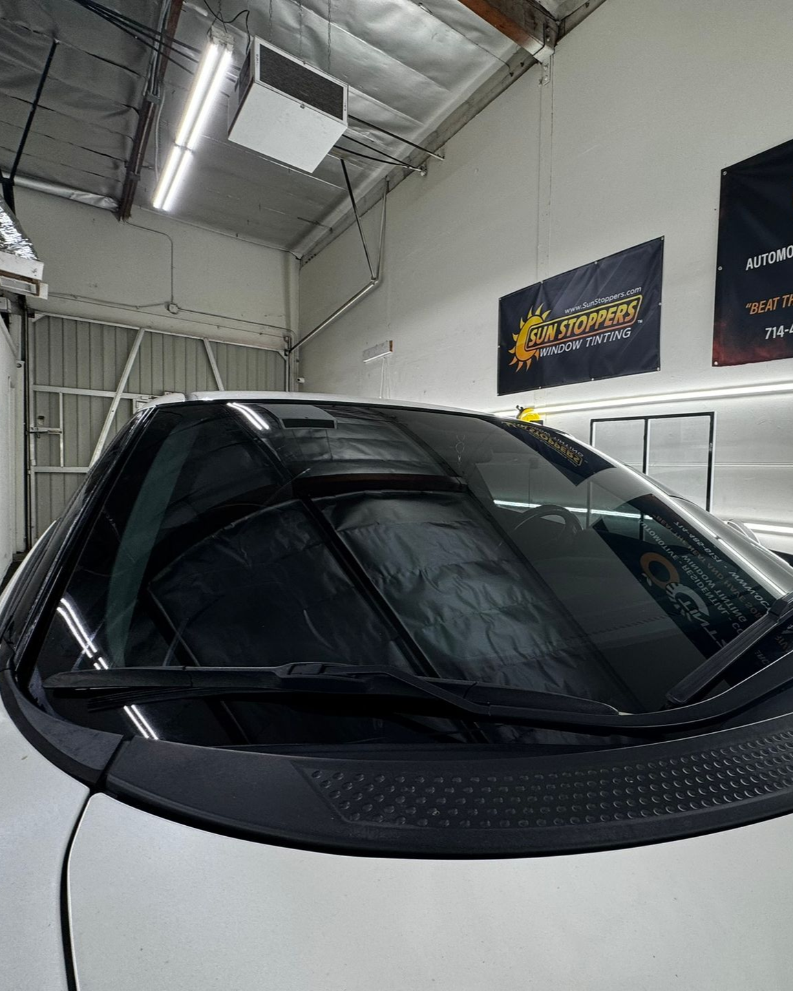 White car in a garage, with tinted windshield and black wipers.