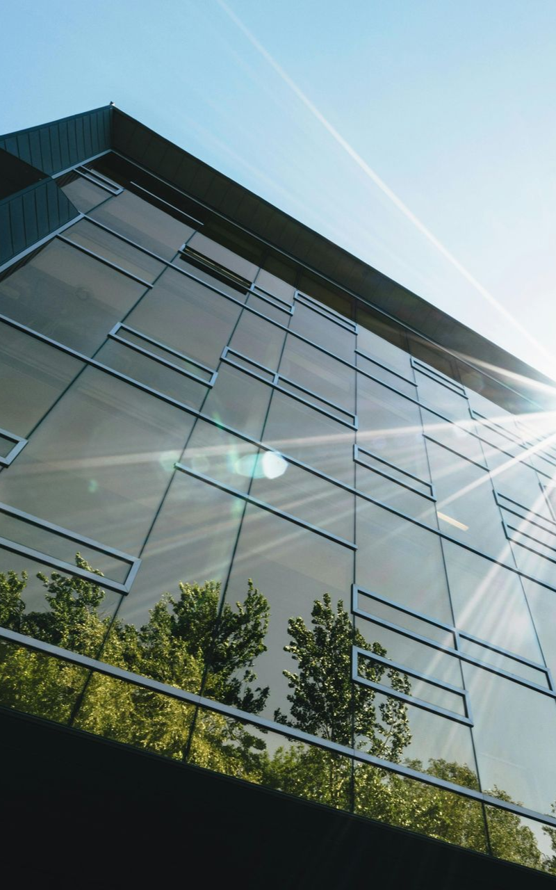 Modern glass building reflects trees against a bright blue sky.