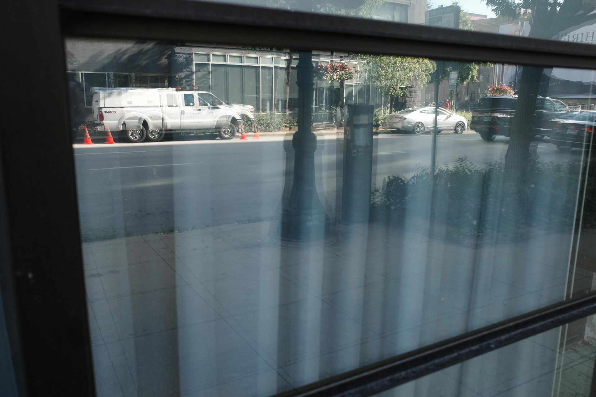 View through window showing street with cars and a service truck parked along the side of a building.