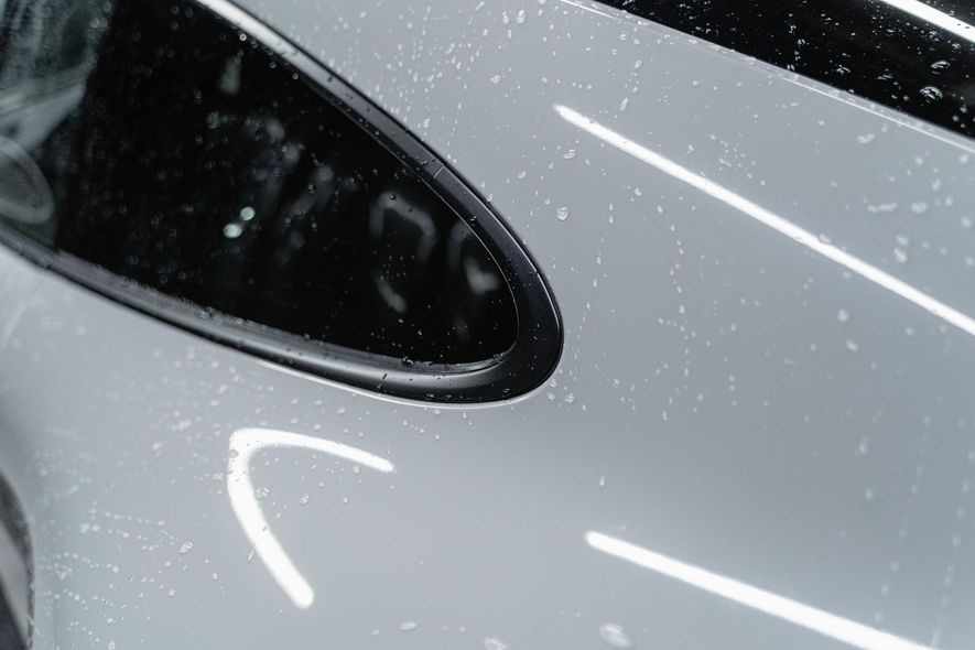 Close-up of a silver car's side vent with water droplets.