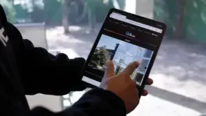 Person holding a tablet, zooming on a map. Dark webpage, outdoor background visible.