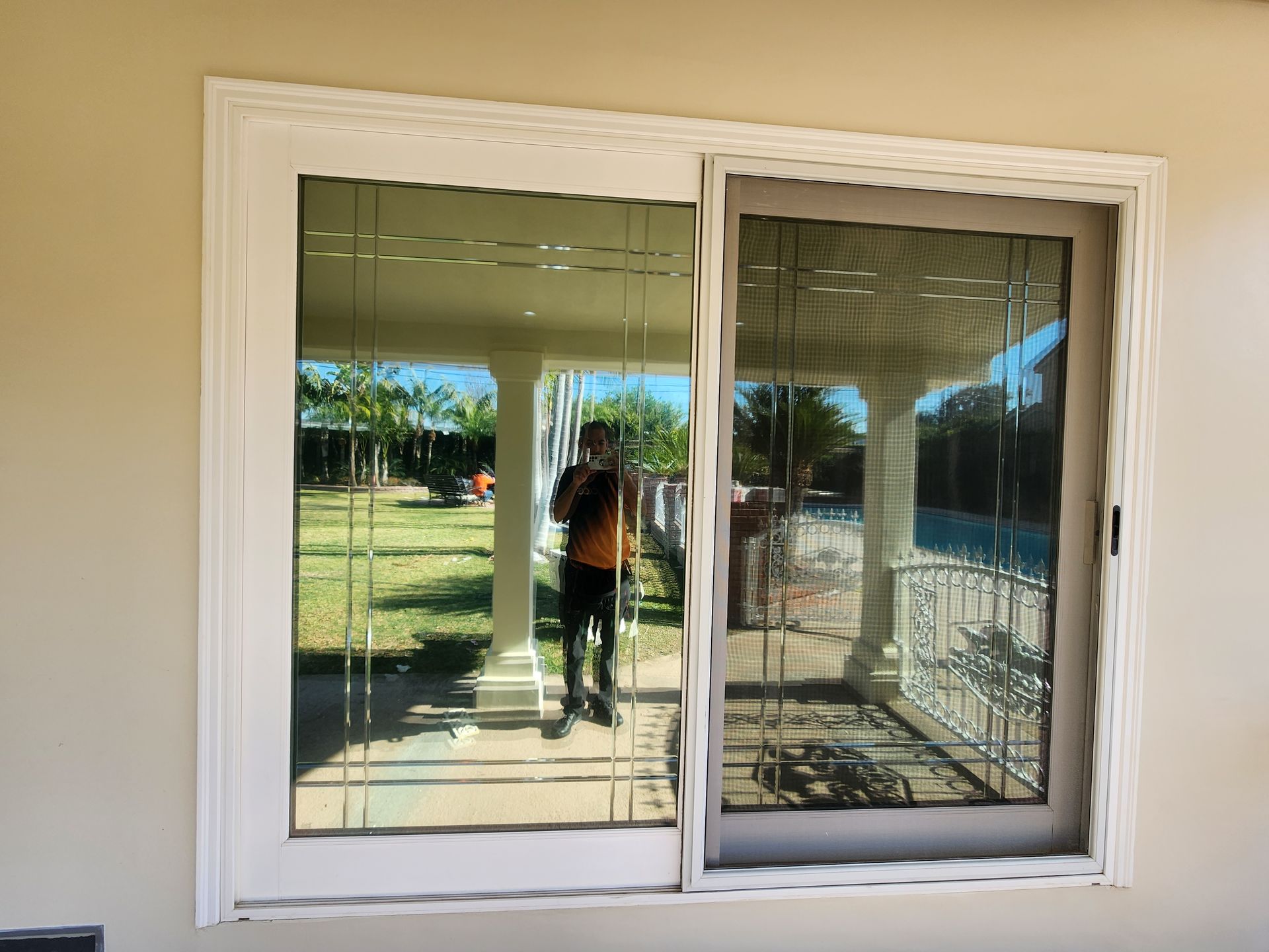 Sliding glass door with white trim, reflecting a person and a porch with columns; set outdoors.