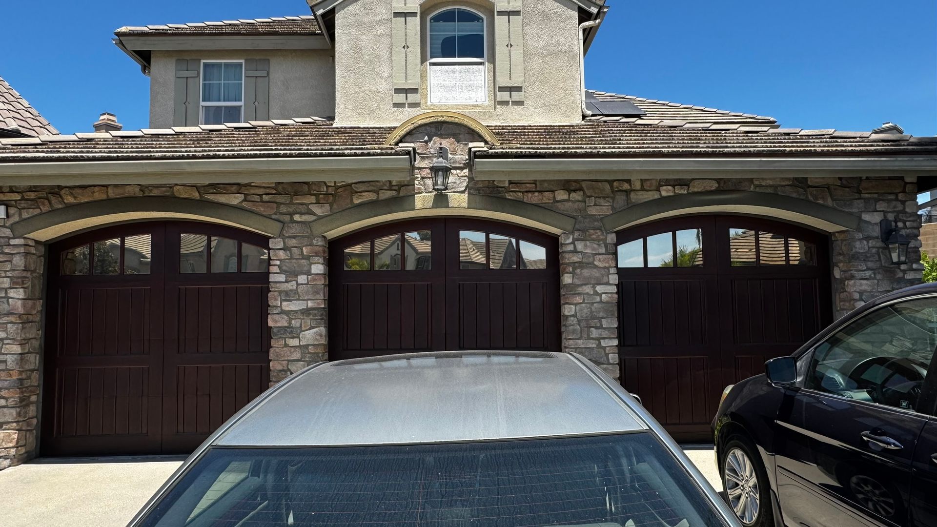Three-car garage with brown doors and stone exterior. A silver car and black car are parked in front.