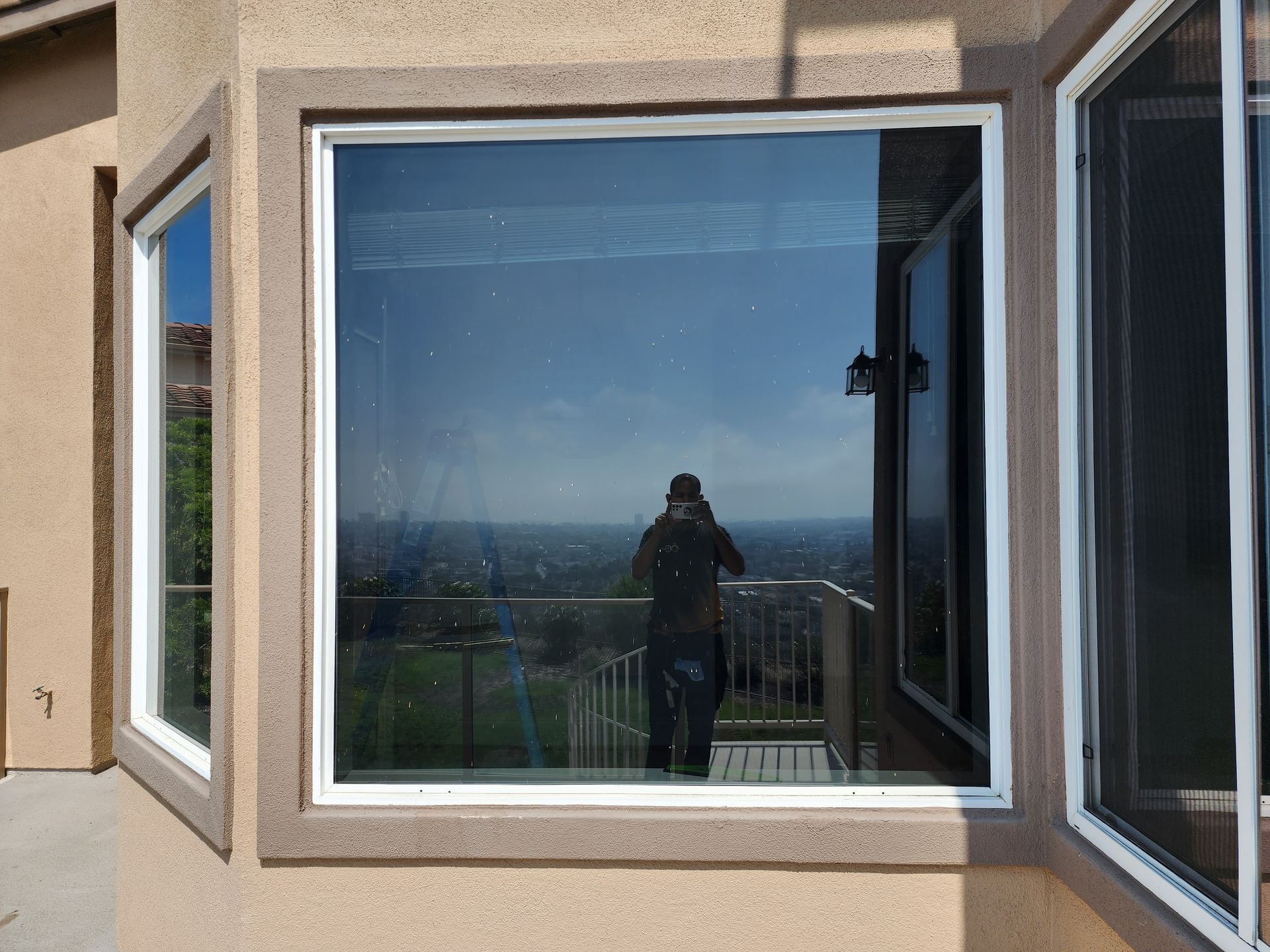 Patio with glass windows and doors reflecting the surroundings; metal chairs, a red trash can.